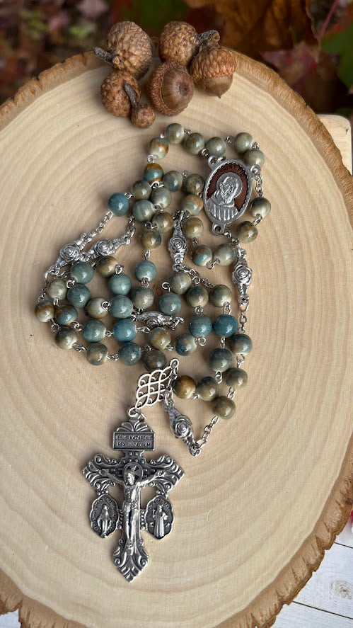 Close-up of earthy ceramic bead rosary with silver crucifix and Saint Pio centerpiece medallion, ideal for prayer and Catholic devotion.