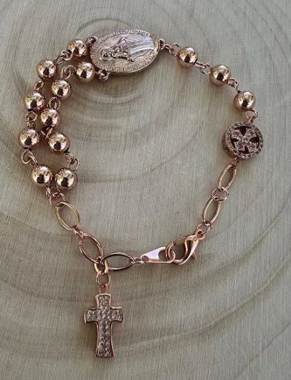 Miraculous Medal rosary bracelet with rose gold beads and cross charm displayed on natural wood background