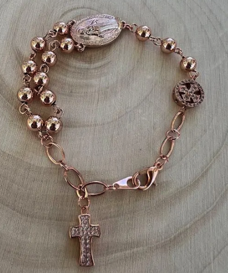 Close-up of handmade Catholic rosary bracelet in rose gold with Marian medal and textured cross charm