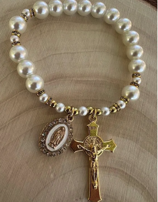 Catholic pearl bracelet with gold-tone Our Lady of Guadalupe medal and crucifix, displayed flat on wooden surface
