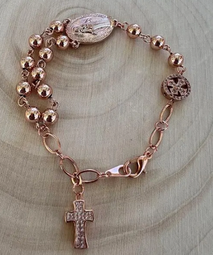 Close-up of handmade Catholic rosary bracelet in rose gold with Marian medal and textured cross charm