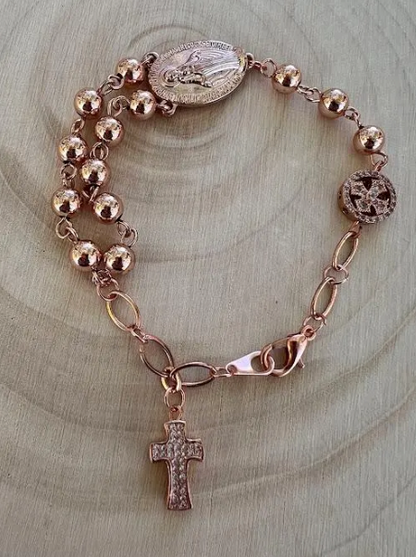 Rose gold rosary bracelet featuring polished prayer beads, Miraculous Medal centerpiece, and lobster clasp